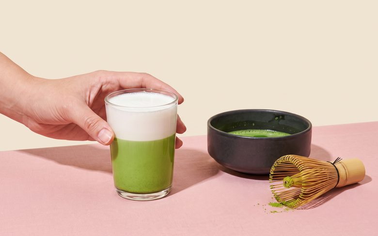 Matcha latte served on a specialty cafe counter beside a whisk and bowl