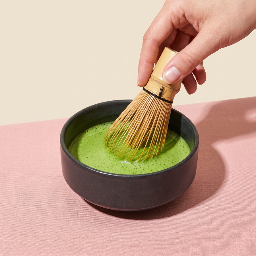 Hand whisking Allreasons matcha in a ceramic bowl with a bamboo whisk